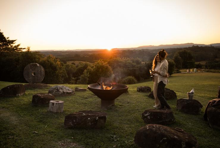 A couple standing beside a campfire on a grassy hill during sunset at Gaia Retreat & Spa, Byron Bay, New South Wales © Gaia Retreat & Spa