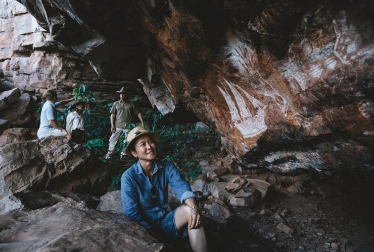 A group of people talking and admiring Aboriginal rock art during a tour with Kakadu Cultural Tours, Kakadu National Park, Northern Territory © Tourism Australia
