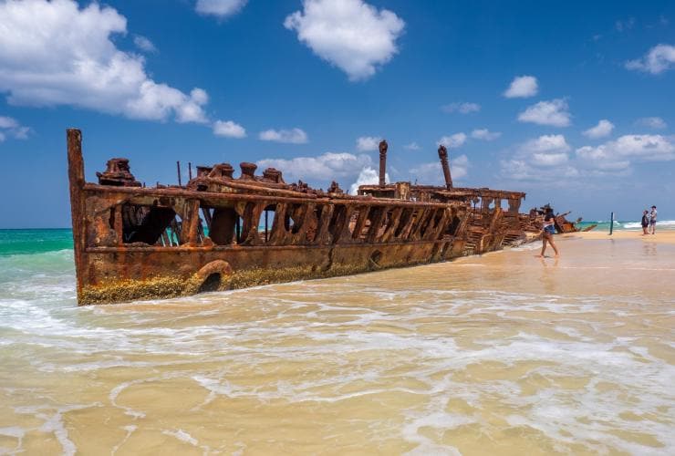 People exploring the ruins of Maheno Shipwreck in the shallow waters of the K’gari coastline in Queensland © Tourism Australia