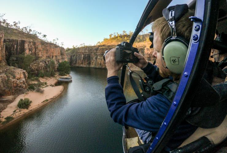 A person snapping a photo from a helicopter window over a picturesque outback gorge, Nitmiluk Tours, Nitmiluk National Park, Northern Territory © Tourism Australia
