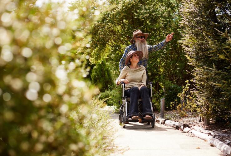 A person in a wheelchair and a tour guide exploring a tree-lined path with Inala Nature Tours, Bruny Island, Tasmania © Tourism Australia