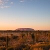 A large red rock monolith rising from the flat outback landscape at Uluru, Uluru-Kata Tjuta National Park, Northern Territory © Tourism Australia