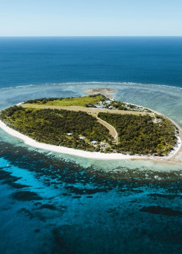  Aerial image of a round, green island with white sand shores surrounded by clear ocean.