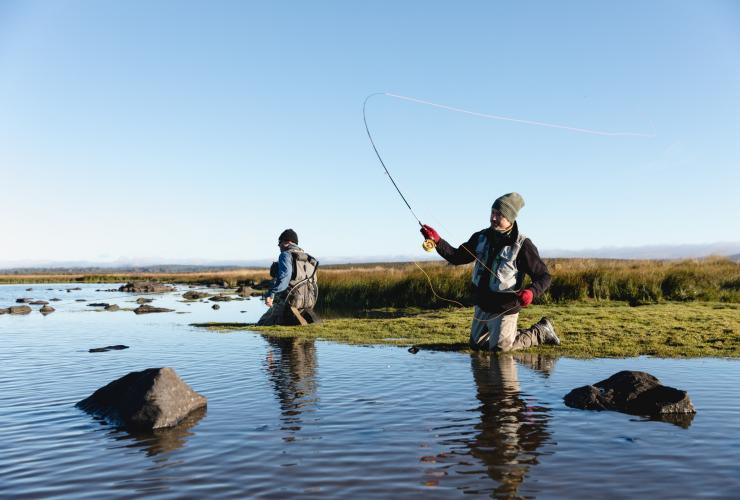 Two people resting on the banks of a waterway while casting fly fishing lines, Lake Burbury, Tasmania © Samuel Shelley