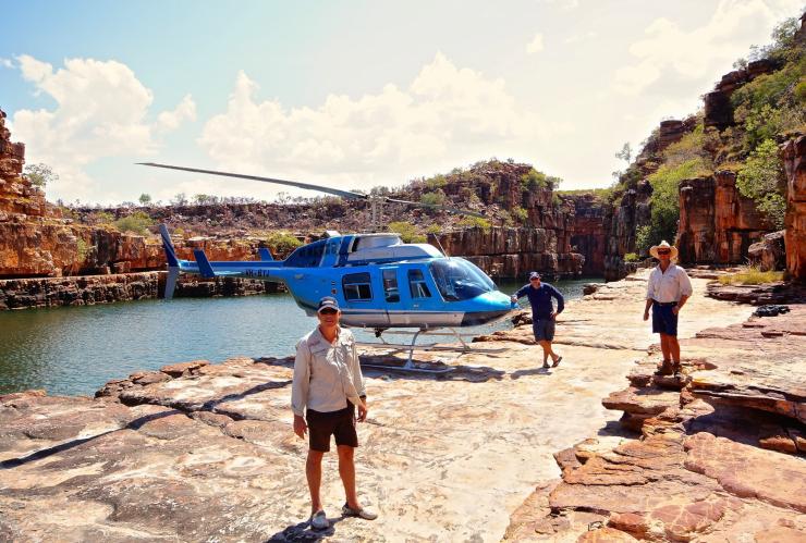 Three men standing beside a helicopter perched on a rocky ledge overlooking a natural waterhole, HeliSpirit, Kimberly, Western Australia © HeliSpirit