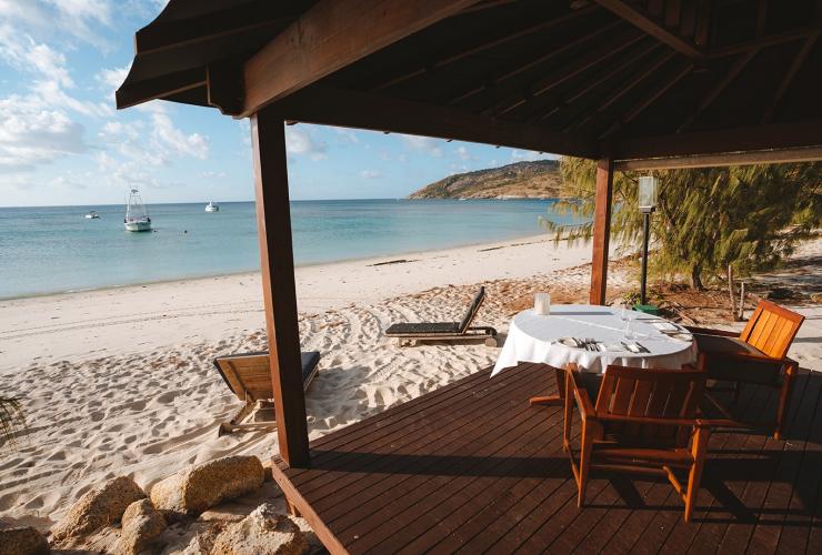 A wooden cabana with a dining table set above white sand leading to the blue ocean at Lizard Island Resort, Lizard Island, Queensland © Tourism Australia