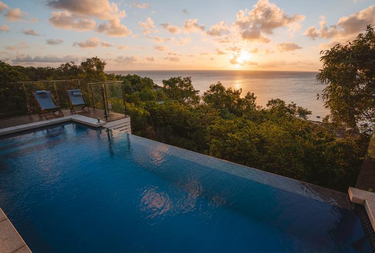 Overlooking a large infinity pool with views over green trees and the sun setting over the ocean beyond at Lizard Island Resort, Lizard Island, Queensland © Tourism Australia