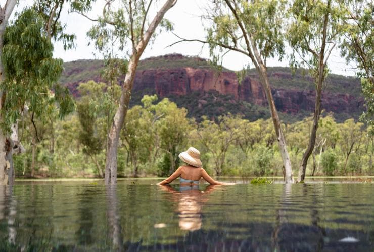 A woman swimming in a pool with the water reflecting surrounding trees and mountains at Mt Mulligan Lodge, Mount Mulligan, Queensland © The Rambler Co