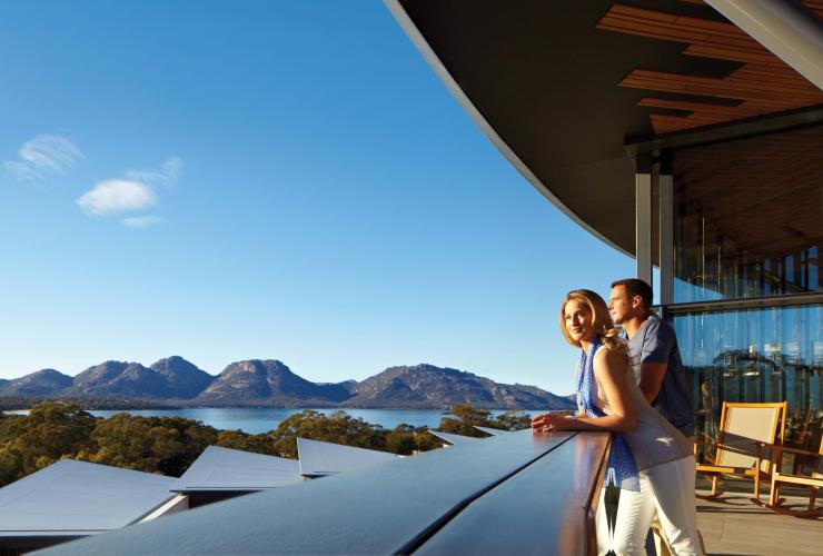 A man and woman leaning over a balcony overlooking Coles Bay, bushland and mountain peaks beyond at Saffire Freycinet, Freycinet National Park, Tasmania © Saffire Freycinet