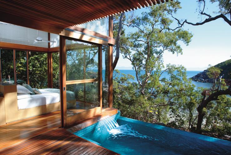 A wooden villa with a bed in a window-lined room beside an infinity pool overlooking bushland and the ocean beyond on Bedarra Island, Queensland © Bedarra Island