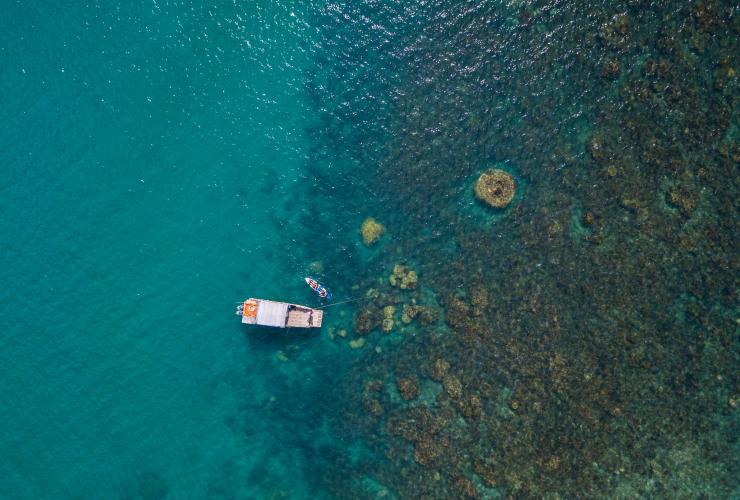 Aerial view over a boat and a person in a kayak beside a reef at Camp Island Lodge, Whitsundays, Queensland © Camp Island Lodge