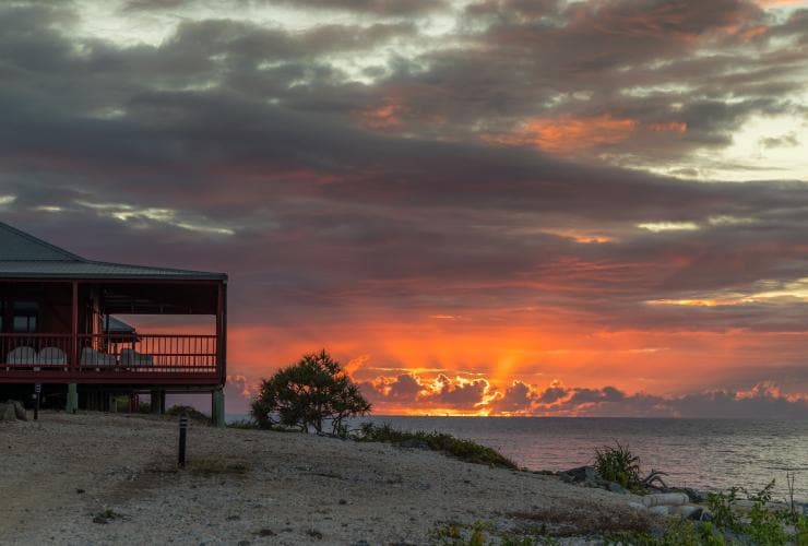 A building on the edge of the ocean beneath a bright orange sunset at Camp Island Lodge, Whitsundays, Queensland © Camp Island Lodge