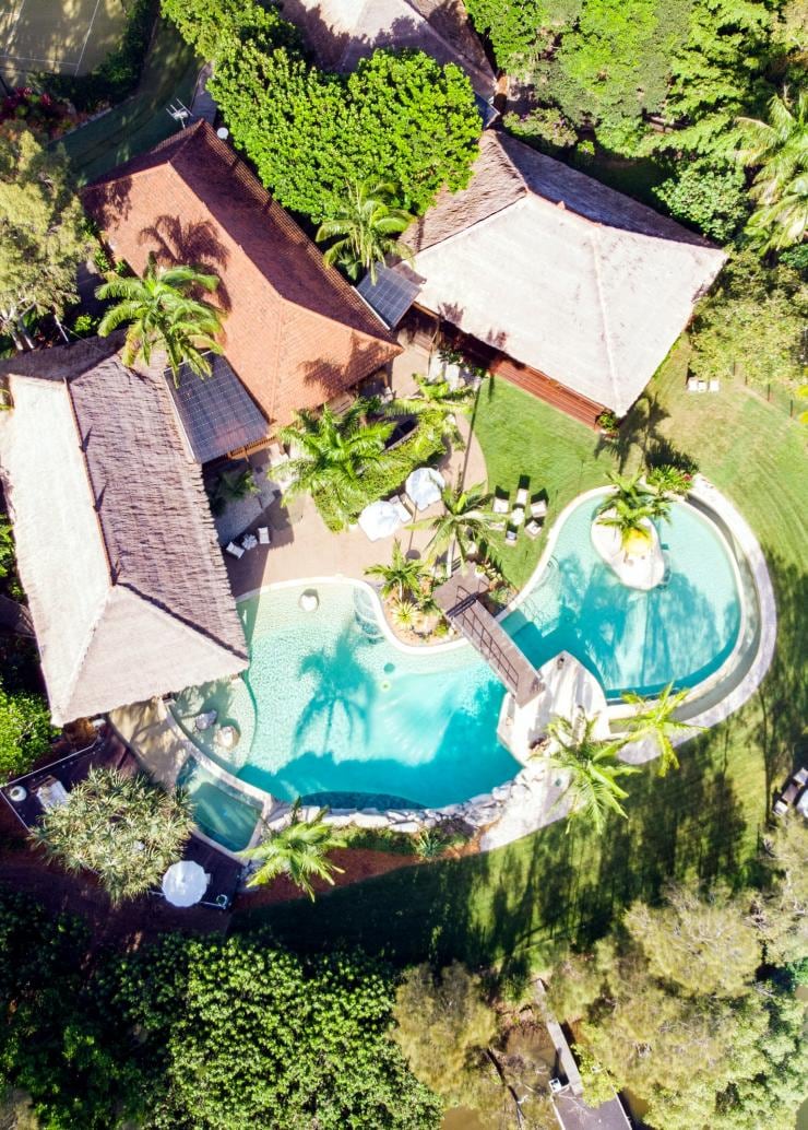 Aerial view over a pool surrounded by trees and villas beside a coastline on Makepeace Island, Noosa, Queensland © Makepeace Island