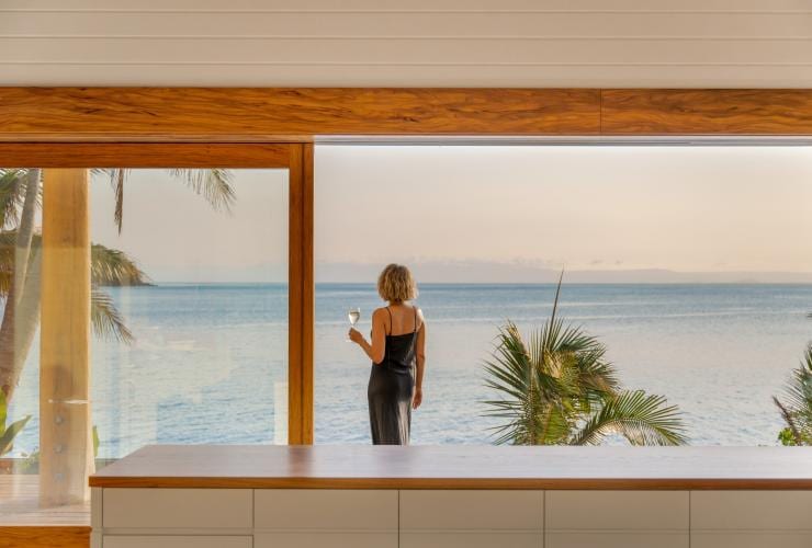 A person standing on a balcony overlooking the ocean with a glass of white wine in hand on Pelorus Private Island, Palm Island, Queensland © James Vodicka/Pelorus Private Island