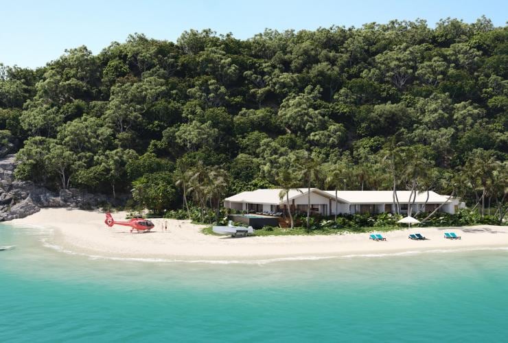 Aerial view over a building bordered by rainforest and a white sand coastline with a red helicopter parked on the sand nearby on Pelorus Private Island, Palm Island, Queensland © Pelorus Private Island
