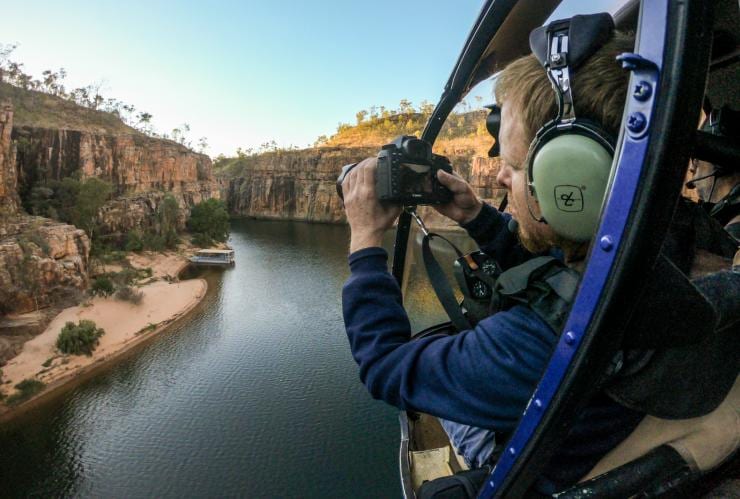 A person snapping a photo from a helicopter window over a picturesque outback gorge, Nitmiluk Tours, Nitmiluk National Park, Northern Territory © Tourism Australia