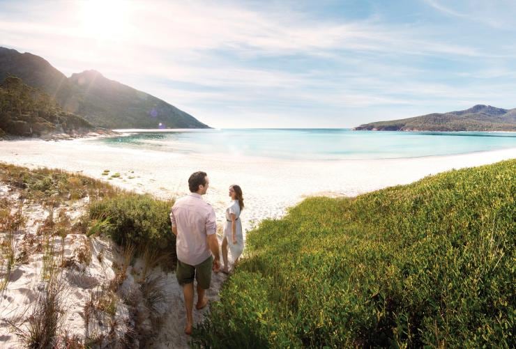A couple walking through bushland approaching the white sand and calm blue water of Wineglass Bay, Freycinet National Park, Tasmania © Myka Photography