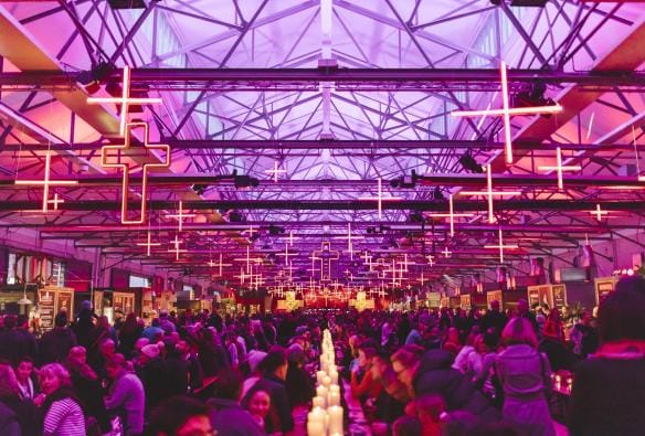 A room filled with people seated at long tables beneath purple and orange lights during Dark Mofo Winter Feast, Hobart, Tasmania © Tourism Tasmania