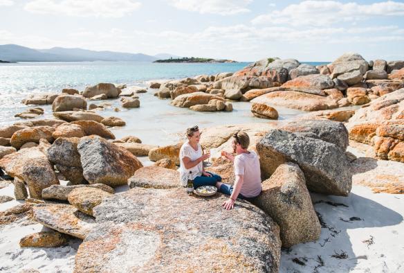 A couple enjoys a picnic on the rocks near Waubs Bay Beach, Bicheno, Tasmania © Stu Gibson