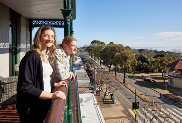 Two guests stand on the hotel room balconies, overlooking the main street of Portarlington and onto the scenic harbour area, Portarlington Grand Hotel, Geelong and the Bellarine, Victoria © Tourism Australia