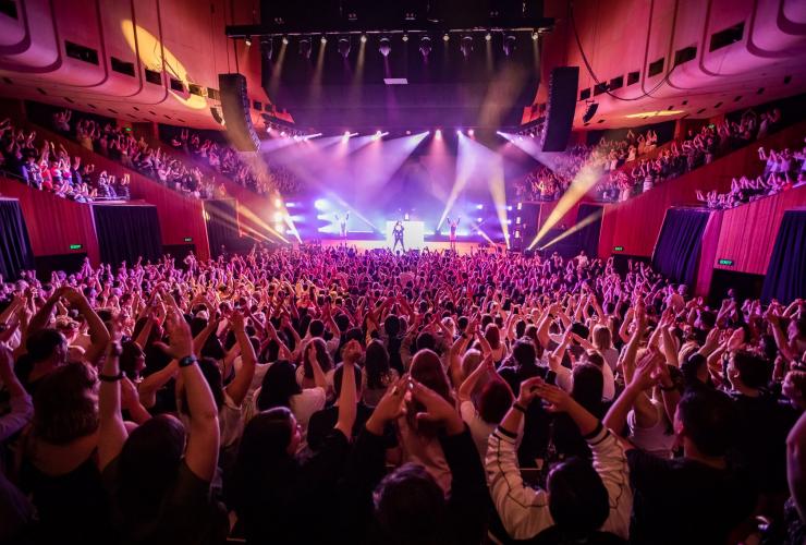 Musical artist Lizzo performing in front of a large crowd with their arms in the air at the Sydney Opera House, Sydney, New South Wales © Daniel Boud