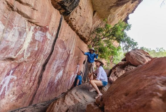 A tour guide with two people crouching on rocks overlooking a cliff face covered in rock paintings with Jarramali Rock Art Tours, Cape York, Queensland © Tourism Tropical North Queensland 