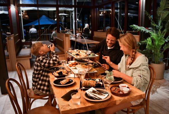 A family talking and laughing at a restaurant while sitting at a table covered with food at Kingfisher Bay Resort, K'gari, Queensland © Tourism and Events Queensland