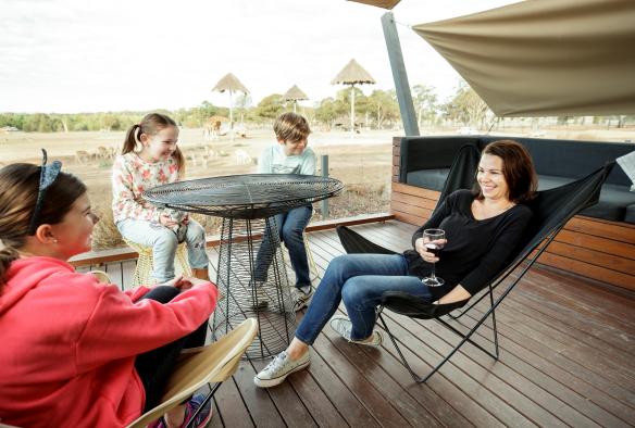 A family sitting on a balcony overlooking a giraffe enclosure at Taronga Western Plains Zoo, Dubbo, New South Wales © Destination NSW