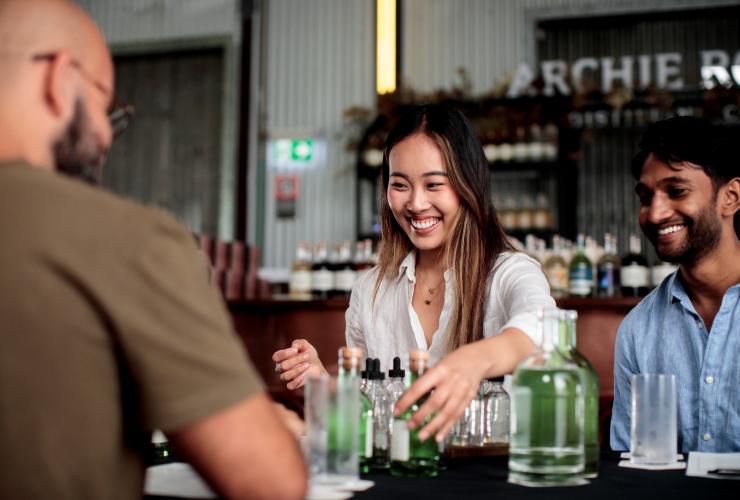 Man and woman smiling while picking up bottles of gin from a table at Archie Rose Distillery, Sydney, New South Wales © Destination NSW