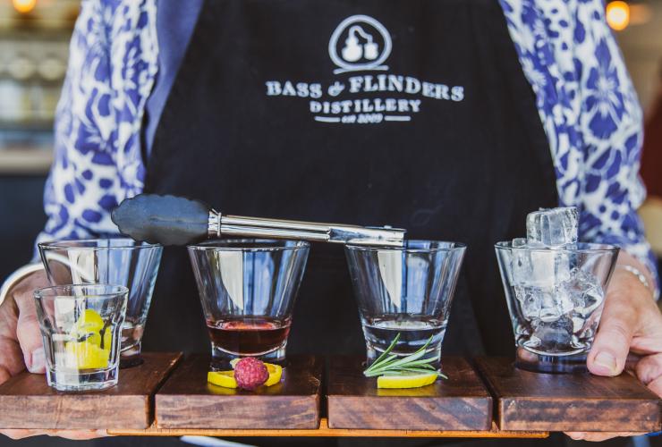 Bartender holding four different spirits on a tray with ingredients in front of them at Bass & Flinders Distillery, Morning Peninsula, Victoria © Bass & Flinders
