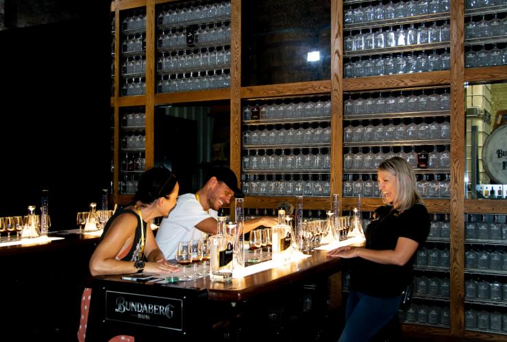Three people laughing around a table of glasses filled with rum at the Bundaberg Rum Experience, Bundaberg, Queensland © Tourism and Events Queensland