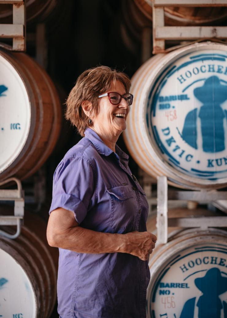 Staff member smiling in front of oak barrels at the Hoochery Distillery Café, Kununurra, Western Australia © Tourism Western Australia