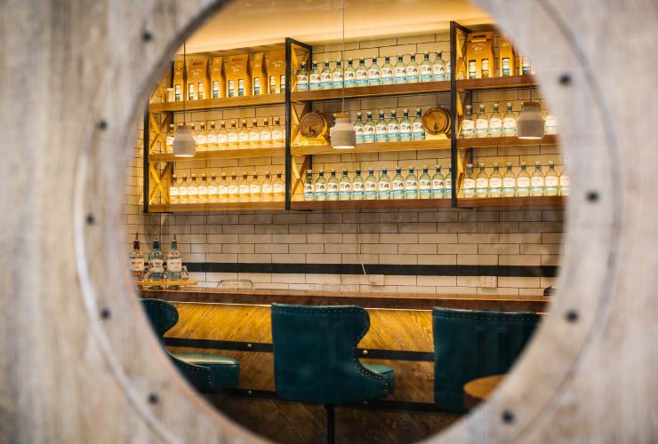 View through a decorative porthole looking at the range of alcohols displayed behind the bar at Manly Spirits Co., Manly, New South Wales © Alana Dimou