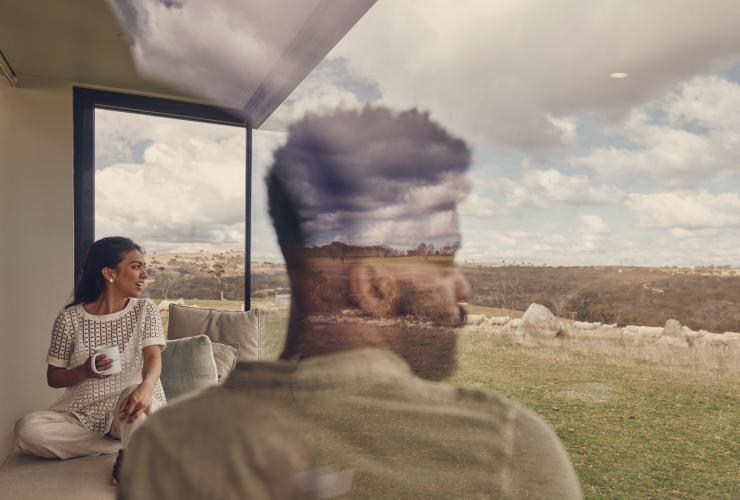 A couple looking out an expansive window of their tiny house accommodation at Wilga Station, Evans Plains, New South Wales © Destination NSW