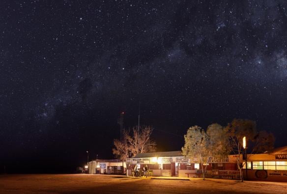 The exterior of a building glowing from lights inside beneath a star-filled sky at night at William Creek Hotel, Flinders Ranges & Outback, South Australia © South Australian Tourism Commission