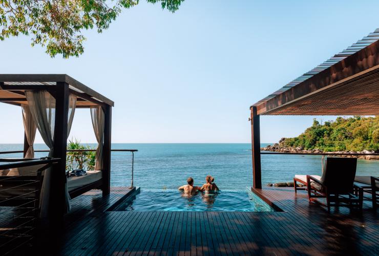 A man and woman swimming in a plunge pool overlooking the ocean and surrounded by a wooden deck with cabanas and daybeds at Bedarra Island Resort, Great Barrier Reef, Queensland © Tourism and Events Queensland