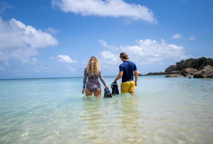 A man and woman walking into clear blue water holding fins and snorkels, Lizard Island Resort, Lizard Island, Queensland © Tourism and Events Queensland