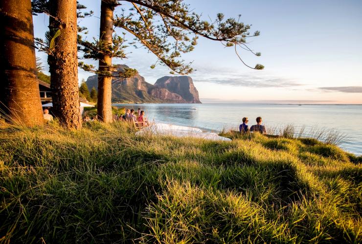 A group of people gathered outside Pinetrees Lodge on the edge of the ocean, Great Walks of Australia, Seven Peaks Walk, Lord Howe Island, New South Wales © Great Walks of Australia/Luke Hanson