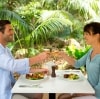 A couple clinking wine glasses over an outdoor lunch surrounded by green trees and plants on a sunny day at Pinetrees Lodge, Lord Howe Island, New South Wales © Destination NSW