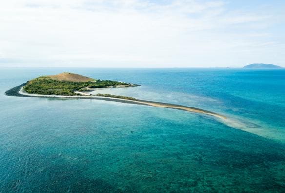 Aerial view over a lush green island surrounded by clear blue water at Camp Island Lodge, Whitsundays, Queensland © Camp Island Lodge