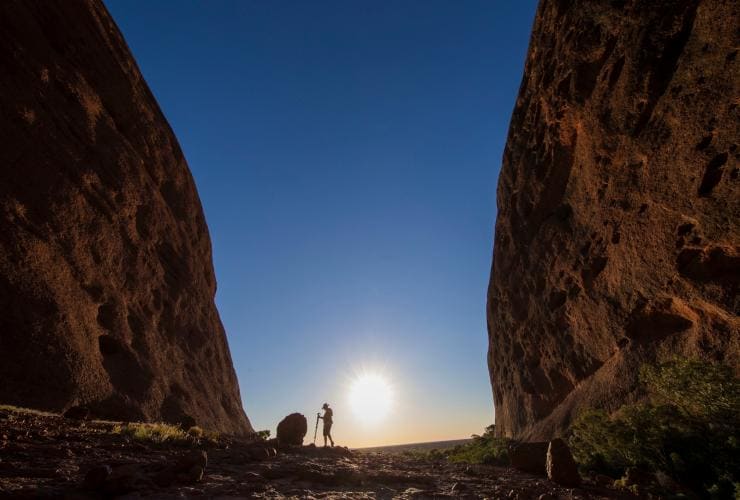 A person standing between two rocky cliffs as the sun begins to set along the Valley of the Winds walk, Kata Tjuta, Red Centre, Northern Territory © Tourism NT, Sean Scott