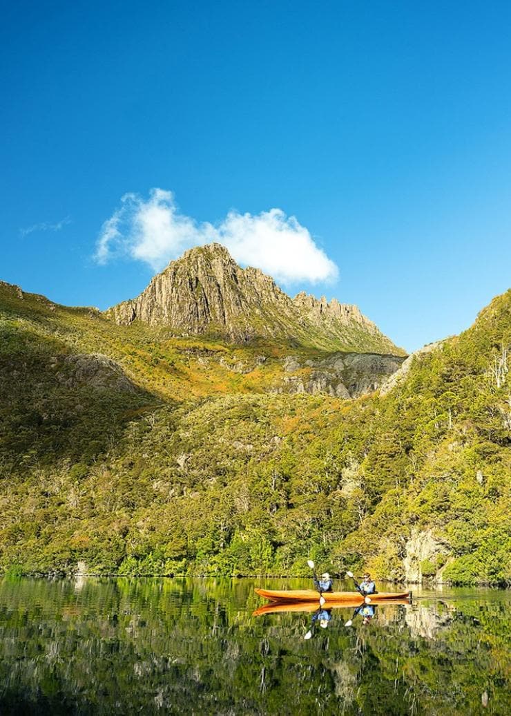 Two people kayaking on a calm lake surrounded by bushland.
