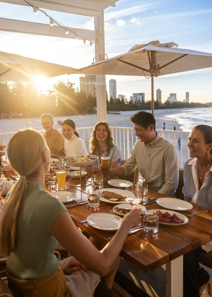 In an open-air dining area at The Tropic at Burleigh Pavilion on the Gold Coast, a group of people enjoy a vibrant meal and refreshing drinks.