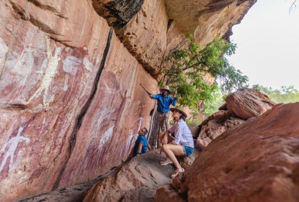 A tour guide with two people crouching on rocks overlooking a cliff face covered in rock paintings with Jarramali Rock Art Tours, Cape York, Queensland © Tourism Tropical North Queensland 