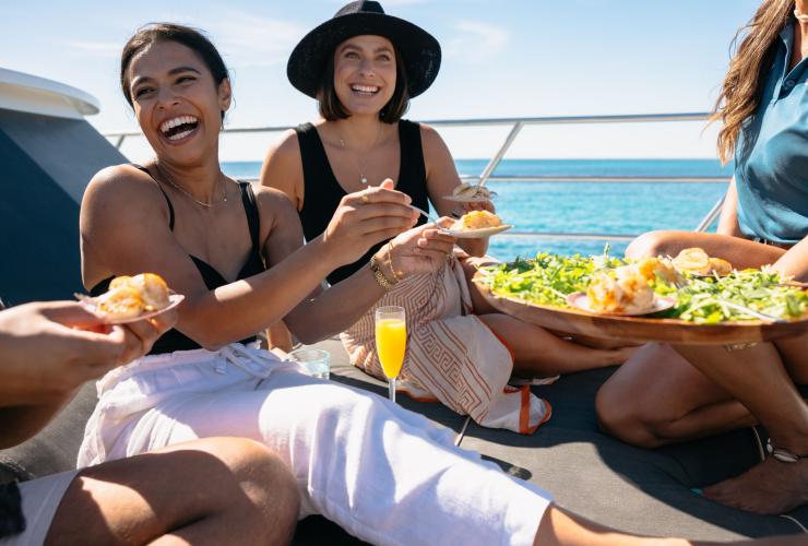 A group of people smiling while enjoying seafood on a boat, Rottnest Cruises, Rottnest Island, Western Australia © Tourism Australia