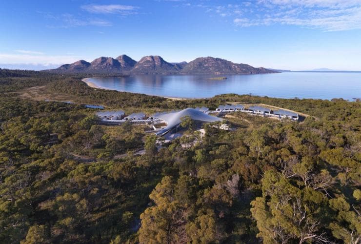 Aerial of Saffire Freycinet accommodation tucked among trees with Coles Bay and Freycinet National Park in the background, Tasmania © Saffire Freycinet