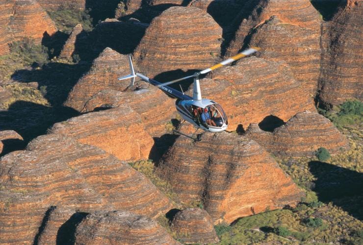 A helicopter flying over large rock domes, Bungle Bungle Range, Purnululu National Park, Western Australia © Tourism Western Australia