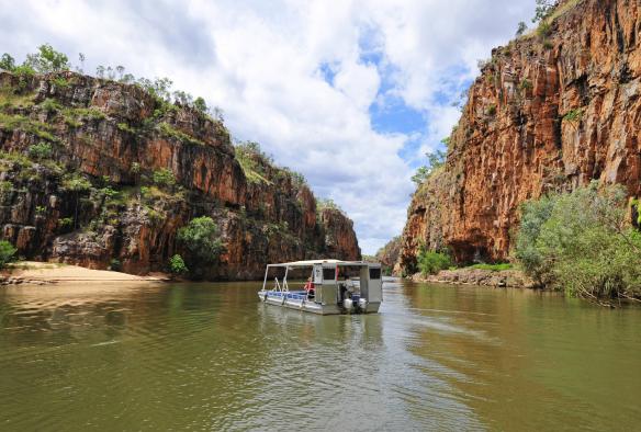 A boat cruising through a gorge with sandy banks and towering orange cliffs, Katherine Gorge, Nitmiluk National Park, Katherine region, Top End, Northern Territory © Tourism Northern Territory