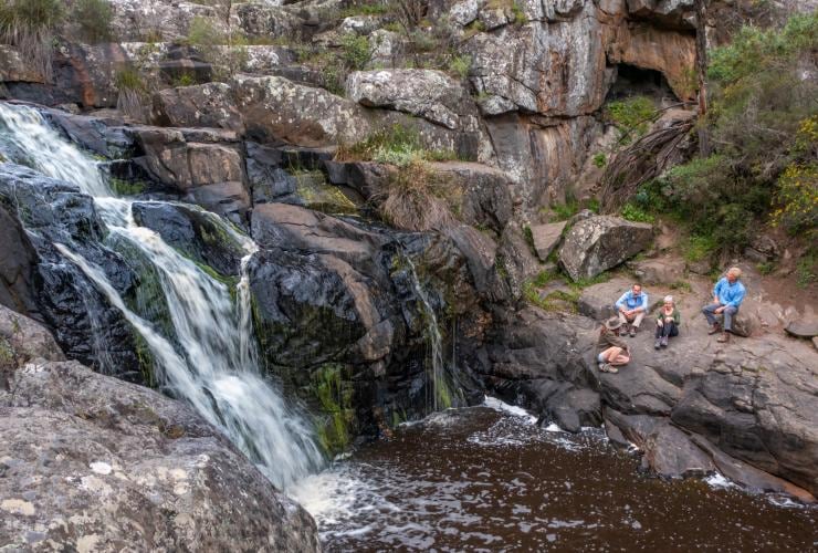 Four hikers taking a break with a waterfall pouring over rocks to their left on the Southern Ocean Walk in South Australia © Tourism Australia
