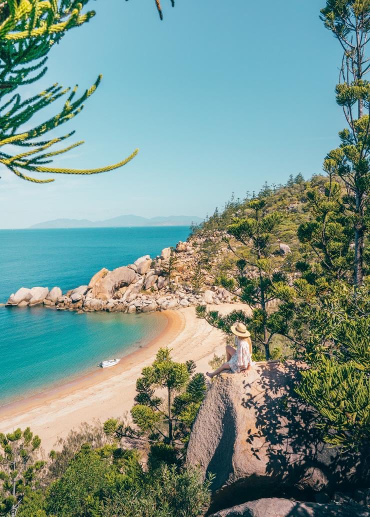 A person sitting on a rock amid green trees overlooking a golden beach, Arthur Bay Lookout, Magnetic Island, Queensland © Townsville Enterprise